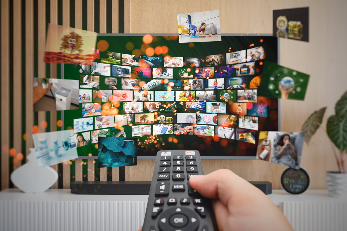 Hand holding a remote aimed at a TV displaying a collage of tiny photos and videos.