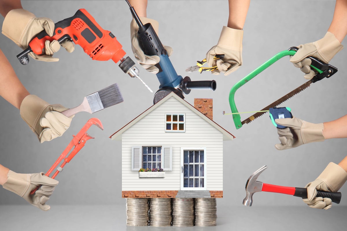 Small house on stacked coins surrounded by gloved hands wielding renovation tools (drill, saw, hammer).”,